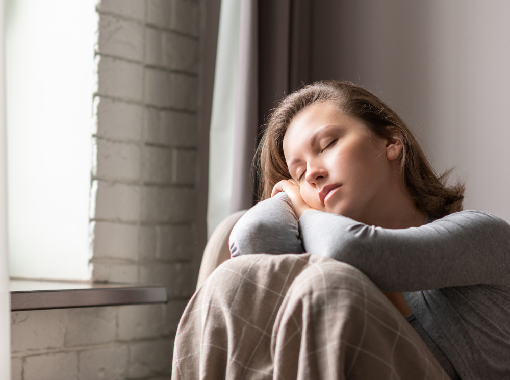 A woman feeling warmth and comfort near the window.