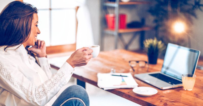 A woman drinking coffee while working on her laptop in a cold office