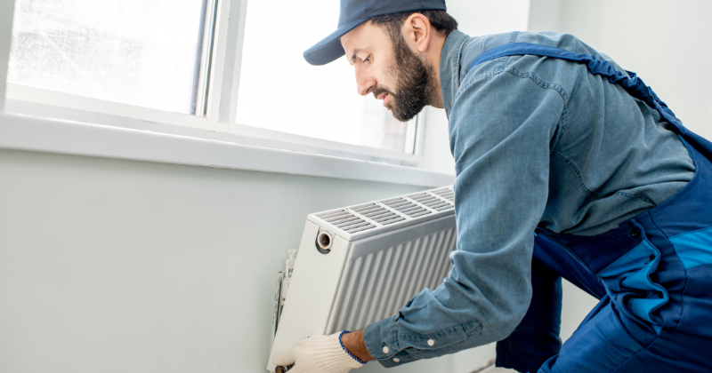 A man is working on installing a wall-mounted electric radiator on the wall