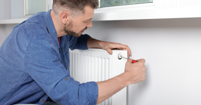 Man installing a wall-mounted electric radiator on a white-painted interior wall.