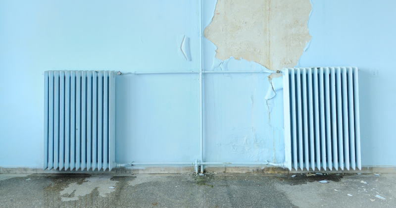 Wall-mounted electric radiator affixed near an exterior blue-painted wall.