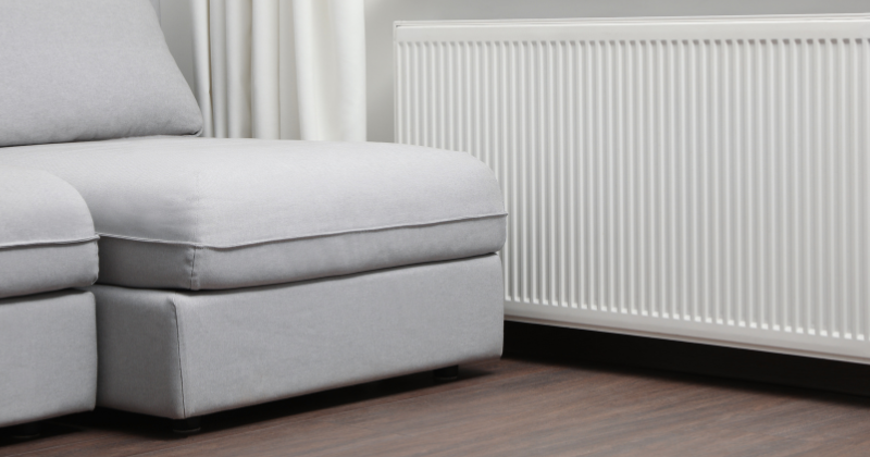 Wall-mounted electric radiator situated near sofa furniture.