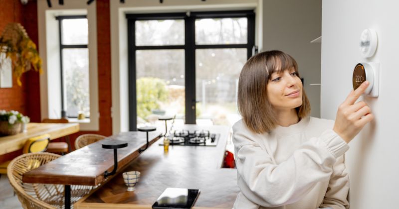 Woman controlling her smart thermostat for her home during the winter season to save energy.