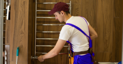 A man installing a wall-heated towel rail on a brown-walled bathroom.