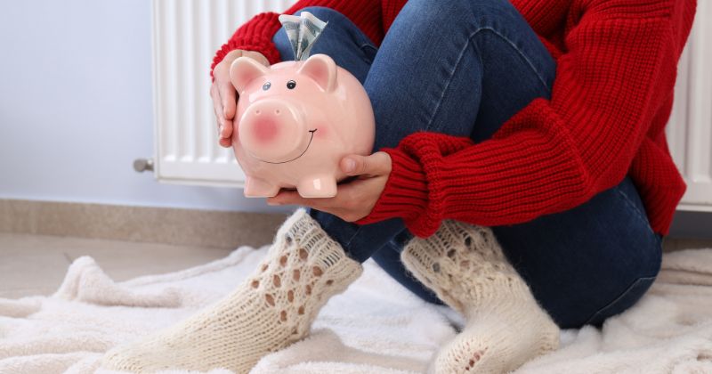 A woman holds a piggy bank while dressed in winter clothing.