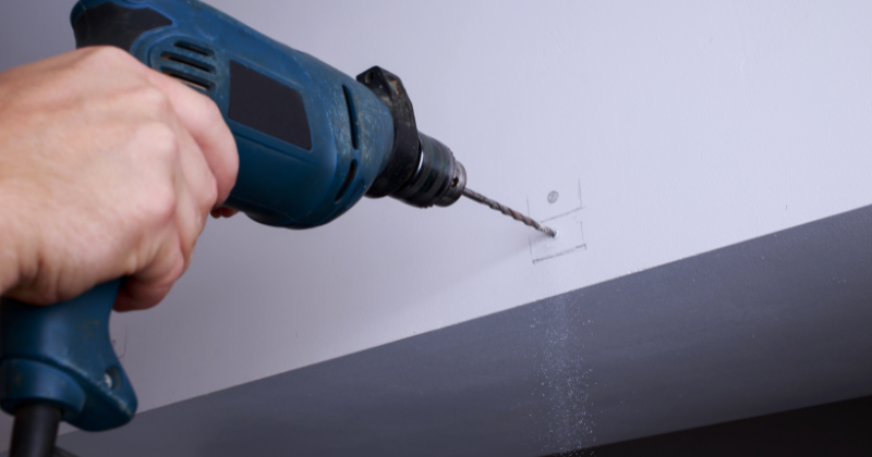 A man drills the wall to install a heated towel rail.