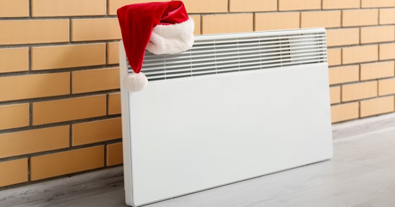 Electric radiator mounted on a brick wall with a Santa hat atop it.