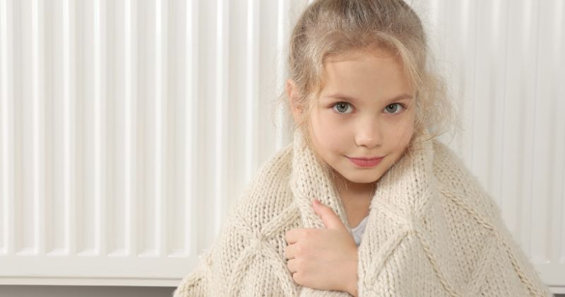 A young girl warming herself with an energy-efficient electric radiator