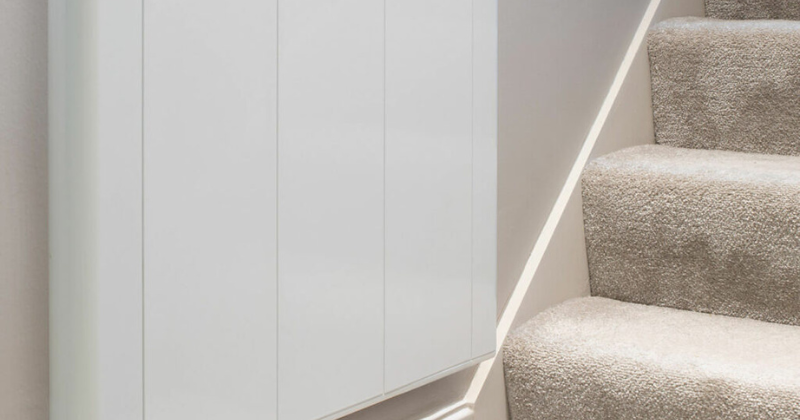 White wall-mounted electric radiator near an elegant staircase.