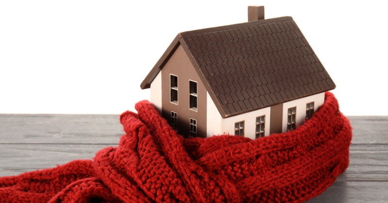 Wooden house figure wrapped in red shawl for warmth.