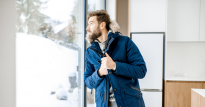 Man feeling cold, gazing through window during winter.