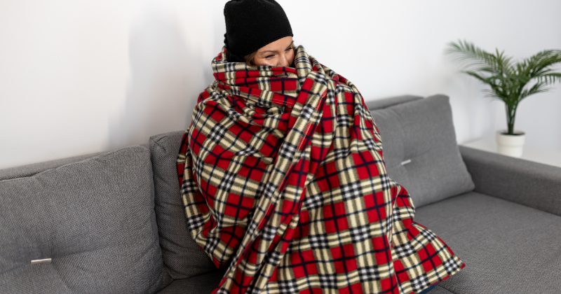 Woman wrapping red blanket, feeling cold in living room.