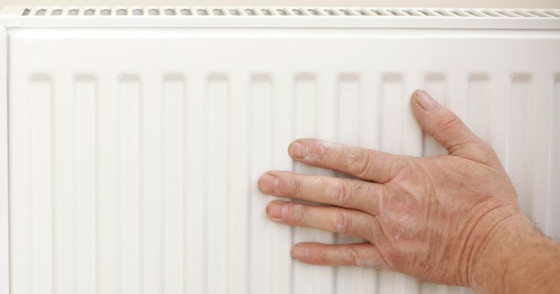 Elderly person's hand exploring texture of electric radiator.